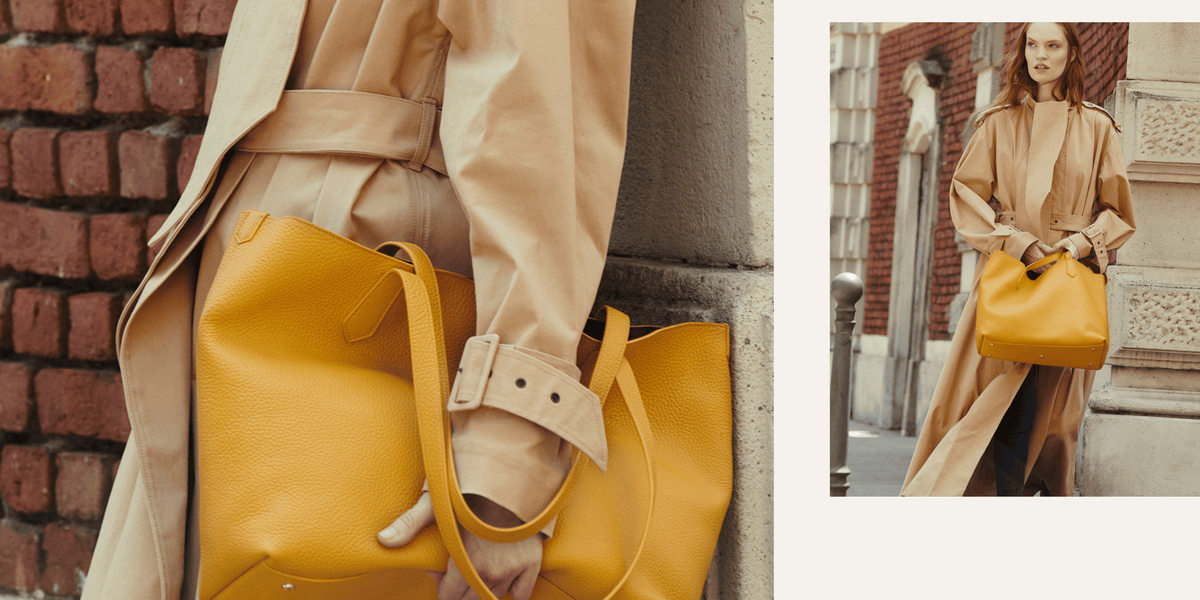 A model in a beige trench coat carries a large mustard yellow leather tote bag, shown in a close-up and a full-body outdoor shot against a brick building.